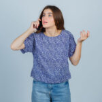 young girl in blue patterned t-shirt, jeans talking to phone, stretching hand as holding something and looking focused , front view.