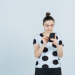 young lady searching something on mobile phone in t-shirt, jeans and looking focused , front view.