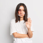 Stop domestic violence. Serious unhappy stressed Asian woman with traces of beating on face keeps palm forward camera has bruise under eye stands indoor. Social problems aggression abuse concept