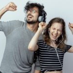 young beautiful couple man and woman with headphones enjoying music dancing standing over white background