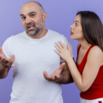impressed-adult-couple-man-looking-showing-empty-hands-woman-touching-his-shoulder-looking-him