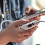 A woman holds a power bank and a phone in her hands.