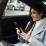 Smiling woman traveling by a car. Businesswoman sitting on backseat of a car and reading text message